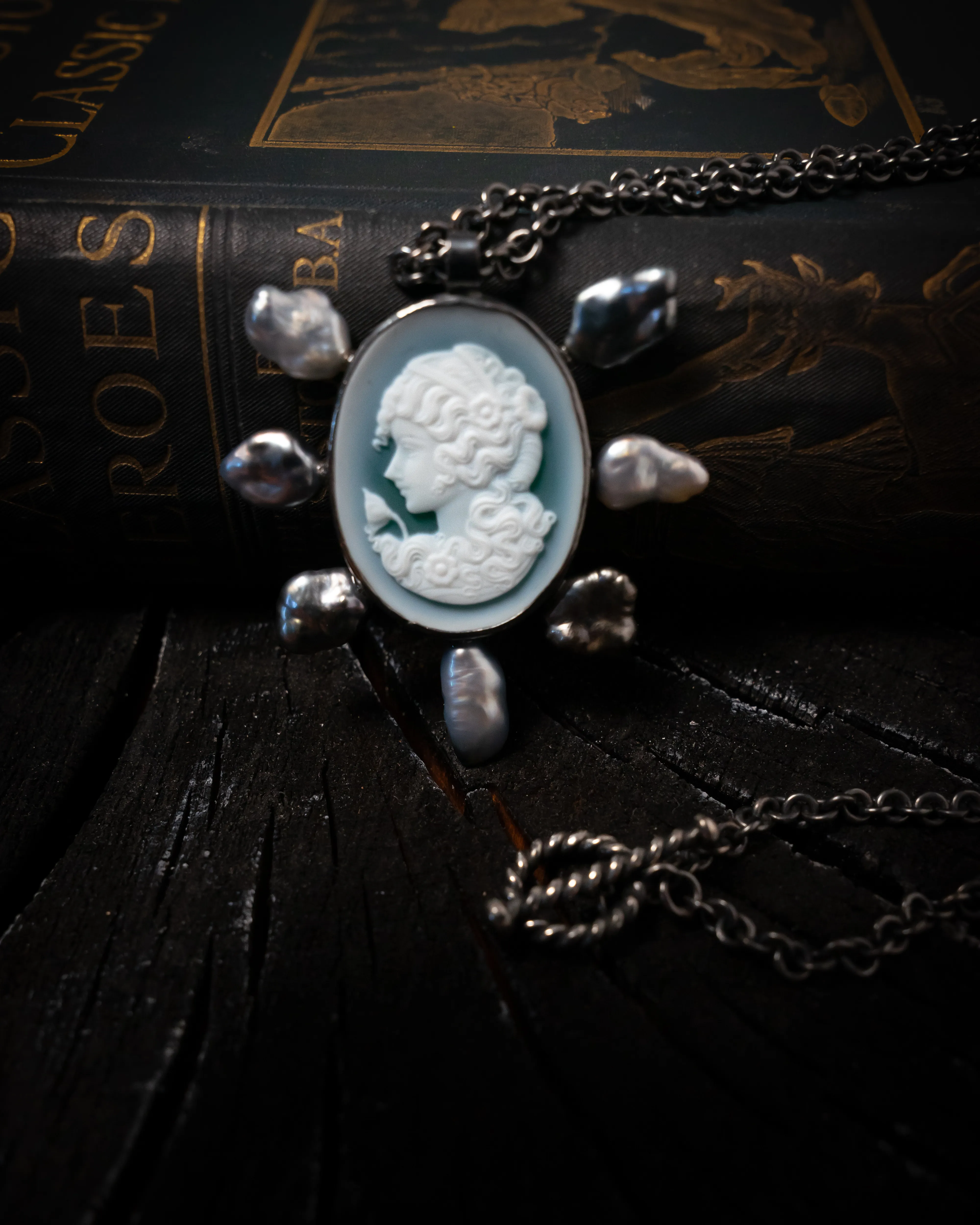 A cameo framed with baroque pearls resting on an antique gilt-lettered book.