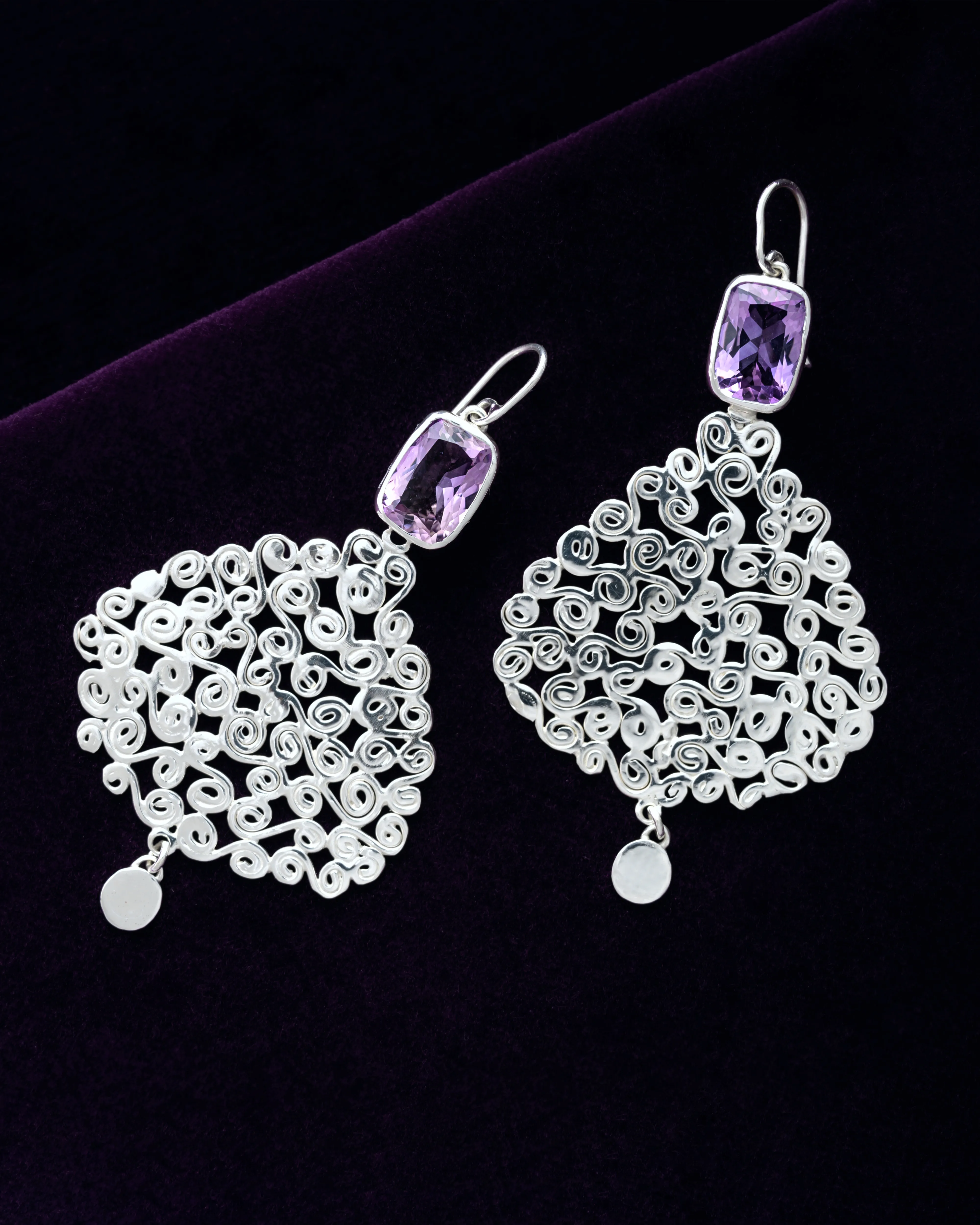 Silver filigree earrings set with step-cut amethysts, resting on deep purple velvet.
