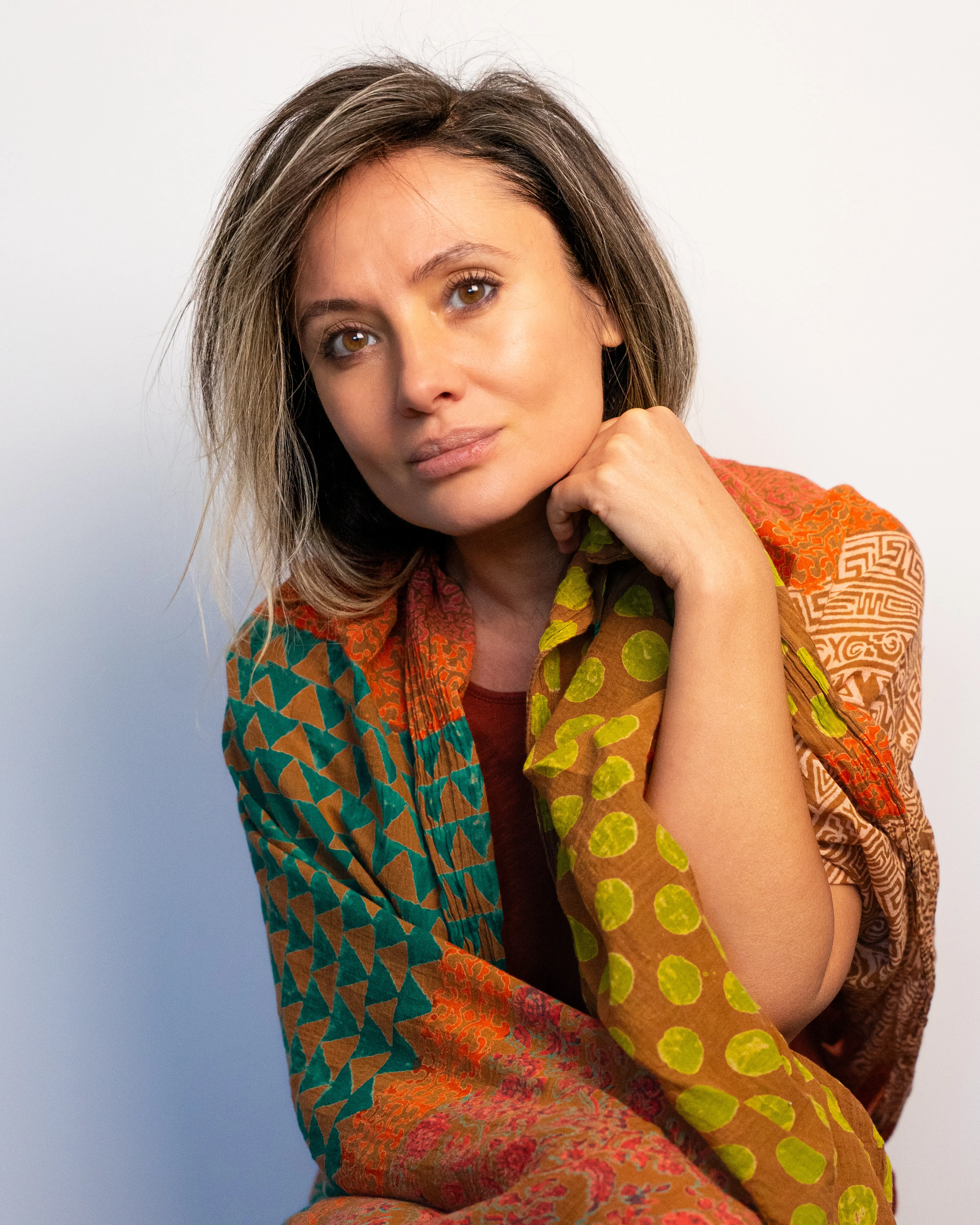 Diana Cernat against a pale wall, wrapped in a patterned silk shawl, her chin resting on her hand as she looks into the camera.